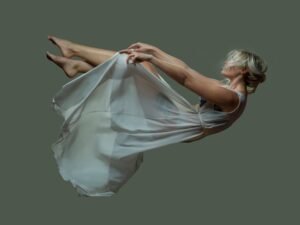 Elegant woman floating mid-air in a sheer dress against a solid background.