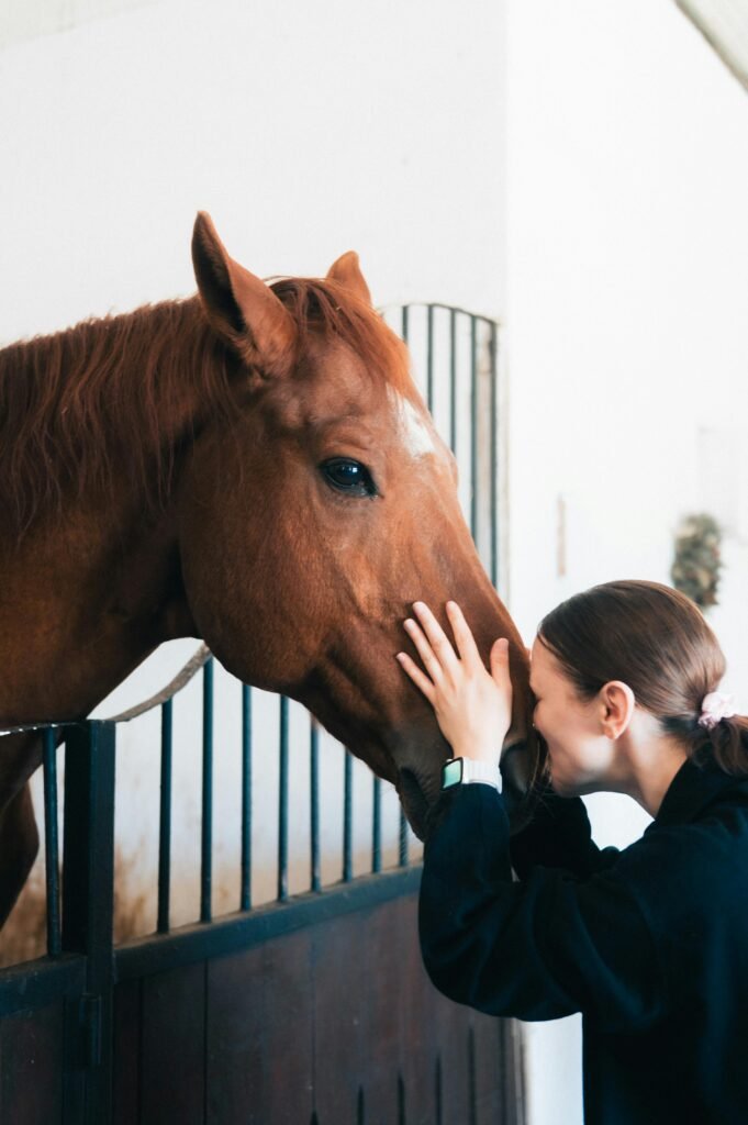 A woman lovingly interacts with a horse in a stable, showing tenderness and connection.